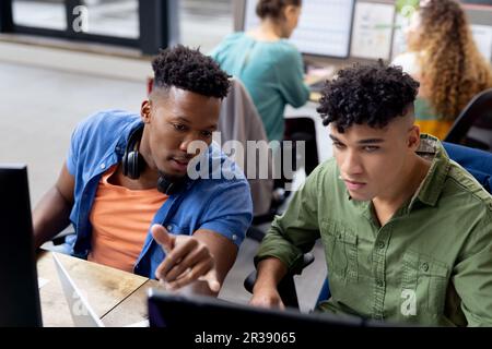 Occupati diversi uomini d'affari alle scrivanie utilizzando computer e parlando in ufficio creativo, inalterato Foto Stock