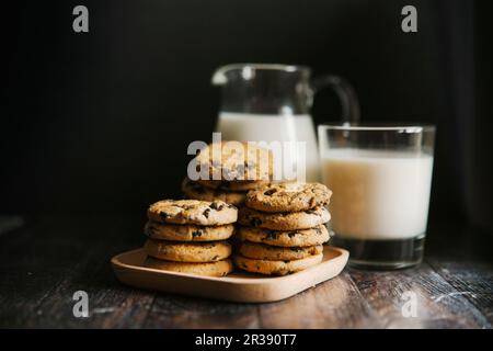 Biscotti al cioccolato, con latte in un bicchiere e caraffa Foto Stock