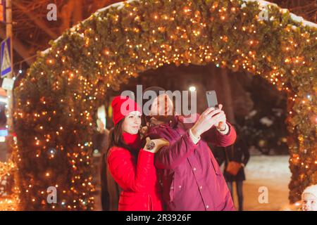 Coppia facendo selfie vicino arco decorato con luci Foto Stock