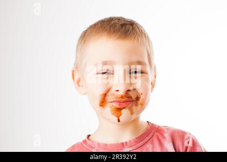 Ritratto del biondo ragazzo con il cioccolato sul suo volto isolato su bianco Foto Stock