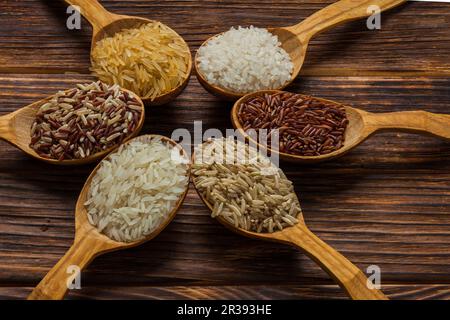 Cucchiai di legno con diversi tipi di riso su fondo di legno Foto Stock