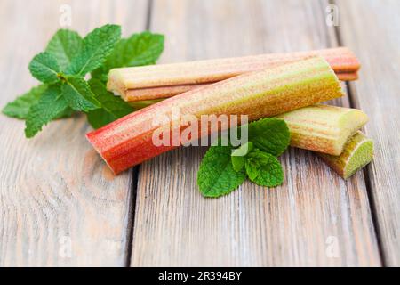 Rabarbaro fresco e foglie di menta su un tavolo di legno Foto Stock