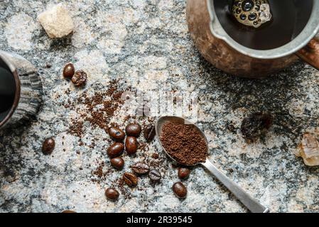 Vista dall'alto verso il basso di chicchi di caffè sparsi, caffè macinato in un cucchiaio, caffè estratto in jezva su una superficie di granito Foto Stock