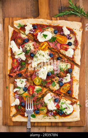 Pizza con mozzarella, pomodori, prosciutto, mirtilli, rosmarino, origano e timo Foto Stock