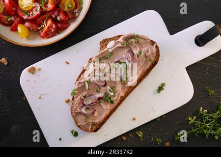 Una fetta di pane spalmata con pâté di fegato e cipolline servite con insalata di pomodoro Foto Stock