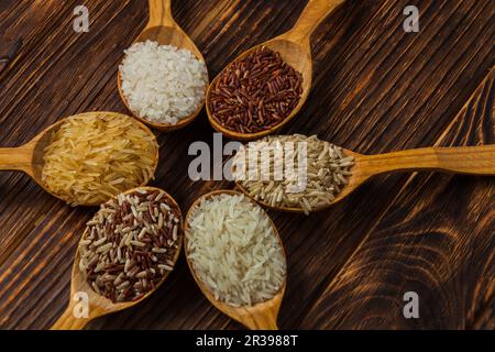 Cucchiai di legno con diversi tipi di riso su fondo di legno Foto Stock