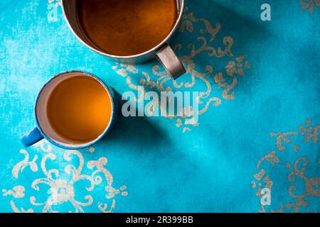 Tè al coriandolo e allo zenzero in una tazza di metallo su una superficie blu azzurro Foto Stock