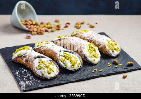 Cannoli siciliani italiani con ricotta dolce, patatine al cioccolato e guarniti con pistacchi tritati e zucchero a velo Foto Stock