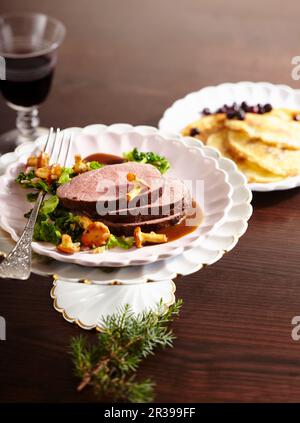 Sella di cervo arrosto con cavolo e funghi finferli e frittelle di mirtilli Foto Stock