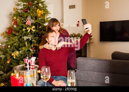 Coppia felice scatta foto a smartphone vicino all'albero di Natale Foto Stock