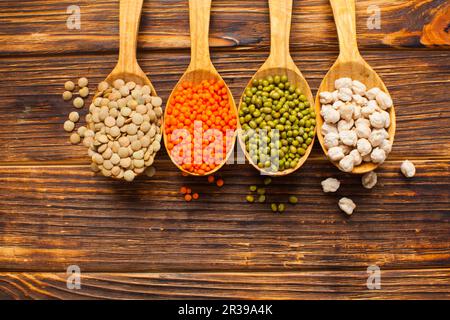 Piano di composizione dei laici con cucchiai colmi di diversi tipi di fagioli su sfondo di legno Foto Stock