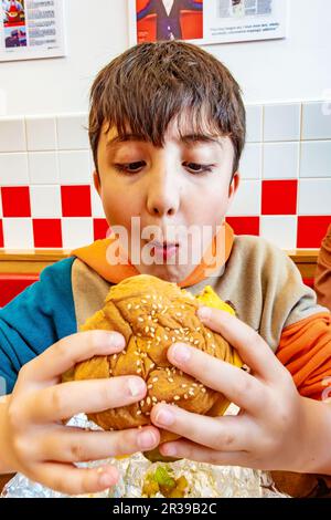 Un ragazzo che mangia un cheeseburger in un ristorante Five Guys Fast Food Foto Stock