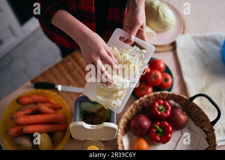 Casalinga cucina insalata sana a casa e gettando cibo avanzi in un contenitore di compost. Donna che ricicla i rifiuti organici in un contenitore con bokash Foto Stock