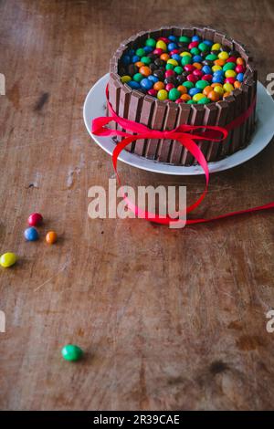 Una torta al cioccolato con barrette di cioccolato su un tavolo di legno con un nastro rosso per la Festa della mamma Foto Stock