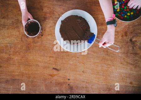 Due bambini che fanno una torta al cioccolato per la Festa della mamma dall'alto su un tavolo di legno Foto Stock