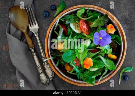 Insalata primaverile, con foglie diverse, vari tipi di pomodori, cetriolo e fiori commestibili Foto Stock