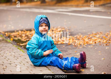 Bambino felice in impermeabile cappotto e rainots all'aperto nella stagione di autunno. Foto Stock