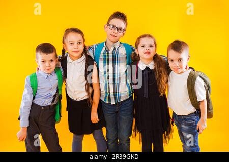 Scolari intelligenti sorridenti e che guardano la fotocamera su sfondo giallo. Ragazzi felici in uniforme scolastica con zaini Foto Stock