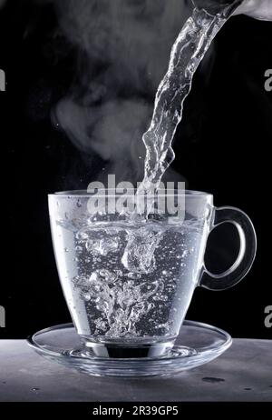 Acqua bollente che è versata in una tazza di vetro Foto Stock