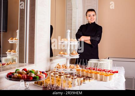 Chef pasticceria in piedi vicino tavola da dessert nel ristorante. Donna fa la presentazione la propria pasticceria e dolci Foto Stock