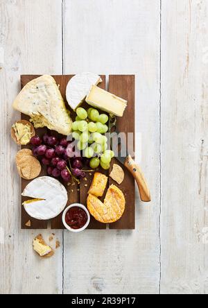 Selezione di formaggi a pasta molle con biscotti, uva e chutney su tavola di legno marrone Foto Stock