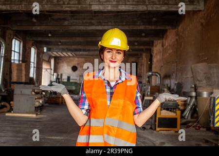 Donna di charme in casco protettivo che accoglie nel suo posto di lavoro Foto Stock