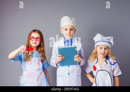 Bambini piccoli cute vestiti come medici su sfondo grigio. Foto Stock