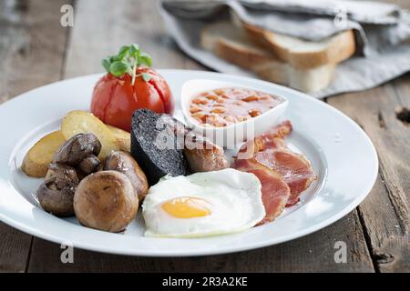 Colazione all'inglese servita su un piatto bianco con pane bianco affettato sullo sfondo Foto Stock