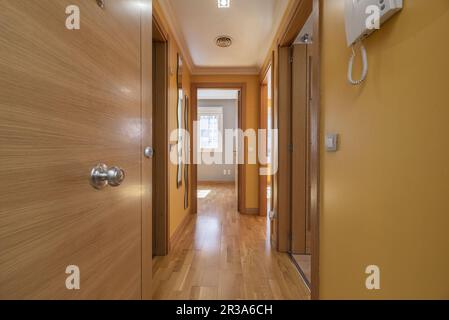 Ingresso di una casa con un lungo corridoio che conduce a diverse camere con porte in rovere e pavimento coordinato Foto Stock