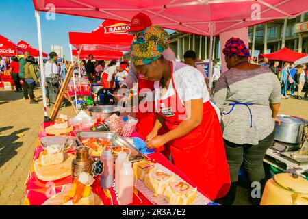 Diversi venditori africani che cucinano e servono vari tipi di cibo di strada a base di pane durante un festival all'aperto Foto Stock