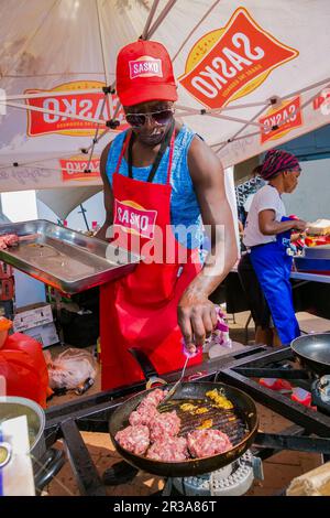 Diversi venditori africani che cucinano e servono vari tipi di cibo di strada a base di pane durante un festival all'aperto Foto Stock