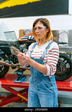 Meccanico femminile che utilizza un tablet digitale trasparente con app per la diagnosi di motociclette Foto Stock