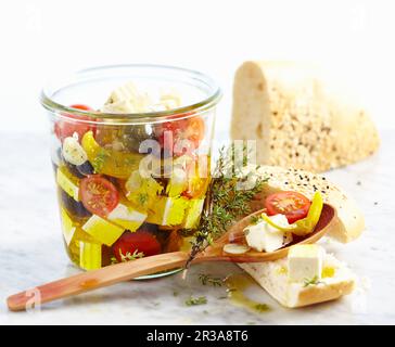 Formaggio feta conservato in olio d'oliva con pomodori, aglio, jalapeno e olive serviti con pane di semi di sesamo senza lievito Foto Stock