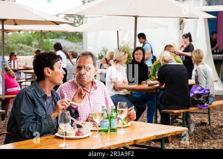 Coppia di mezza età che mangia, beve e in genere che si gode una giornata fuori in una Fiera del cibo e del vino Foto Stock