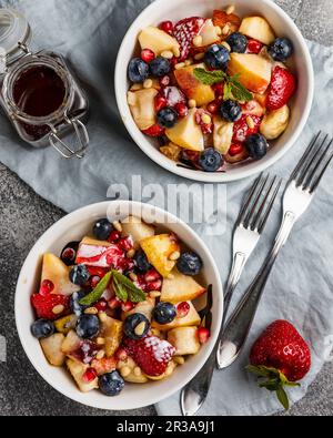 Insalata di frutta con mele, banane, fragole, mirtilli, semi di melograno, pinoli, yogurt e miele Foto Stock