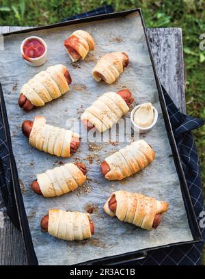 Salsicce avvolte in pasta su una teglia da forno Foto Stock