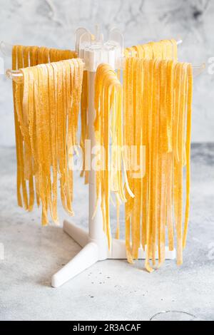 Pasta fatta in casa linguine appeso su rack per asciugare. Tagliatelle italiane fatte in casa appese su un dryi di pasta Foto Stock