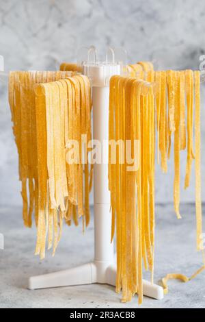 Tagliatelle fatte in casa appese su una griglia per l'asciugatura della pasta. Asciugatura di spaghetti freschi sulla griglia di asciugatura. Se Foto Stock