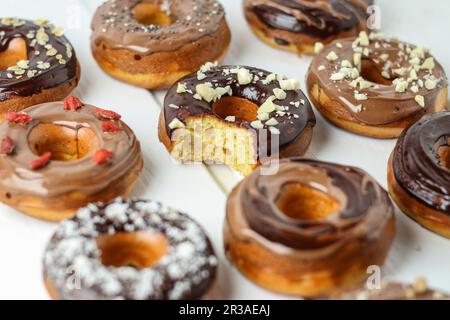 Ciambelle varie con glassa al cioccolato, una con un boccone estratto Foto Stock