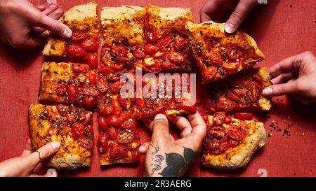 Pizza romana condita con pomodori e peperoni rossi schiacciati con le mani (una tatuata) Foto Stock