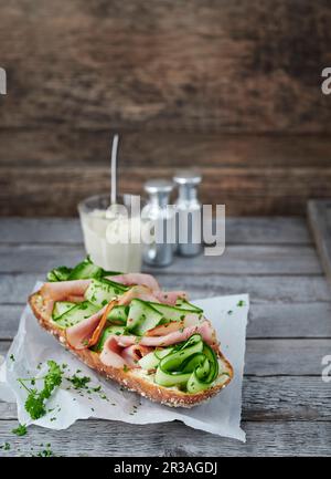 Baguette ricoperta di cetriolo e pancetta su carta antigrasso Foto Stock