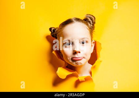 Ragazza piccola curiosa che guarda attraverso il foro in carta gialla. Sconti e vendite stagionali. Foto Stock