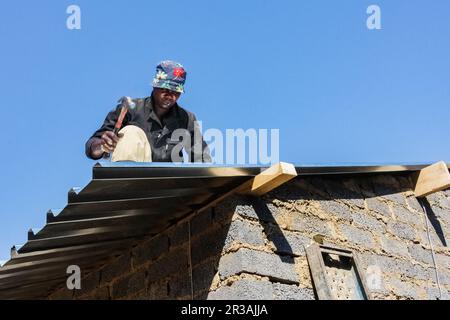 Programma comunitario di Outreach che aiuta a installare tetti in metallo su una piccola casa a prezzi accessibili in una cittadina locale Foto Stock