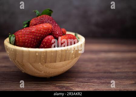 Fragole rosse dolci appena lavate in una ciotola di legno posta su un tavolo. Messa a fuoco selettiva, gocce d'acqua. Foto Stock