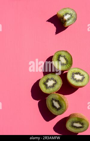 Kiwi si dimezza, uno con un boccone tuso, su una superficie rosa Foto Stock
