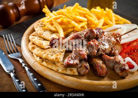 Souvlaki di maiale greco con patate fritte e pane alla griglia Foto Stock