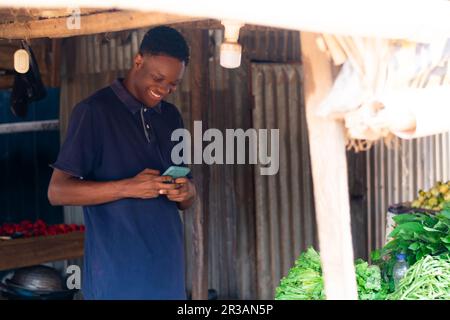 giovane venditore di alimentari nero utilizzando il suo cellulare eccitatamente Foto Stock