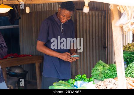giovane venditore di alimentari nero utilizzando il suo cellulare eccitatamente Foto Stock