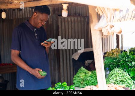 giovane venditore di alimentari nero utilizzando il suo cellulare eccitatamente, facendo pubblicità alla sua attività Foto Stock