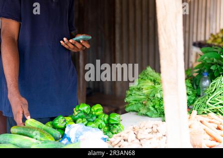 giovane venditore di alimentari nero utilizzando il suo cellulare eccitatamente, facendo pubblicità alla sua attività Foto Stock